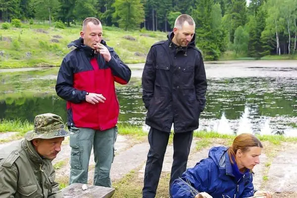 Drei Personen stehen am Ufer eines Gewässers, eine Person arbeitet am Boden