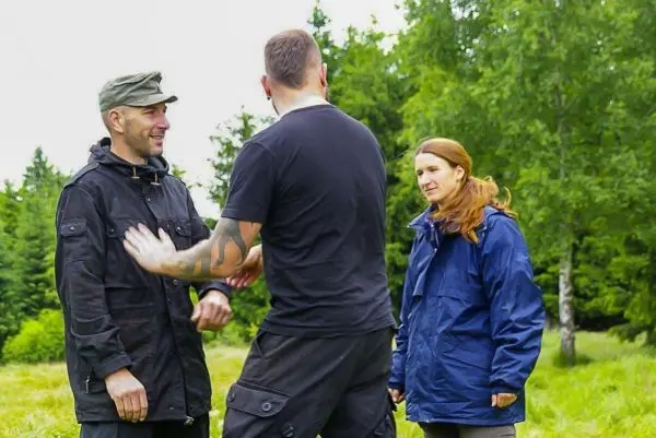 Drei Personen stehen in einer Wiese und unterhalten sich