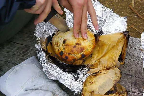 Ein Messer schneidet in ein in Alufolie gewickeltes Brot