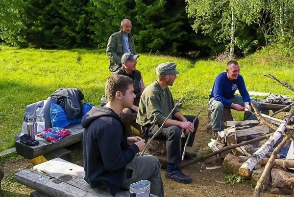 Fünf Personen sitzen um ein Lagerfeuer, Holzstämme liegen bereit