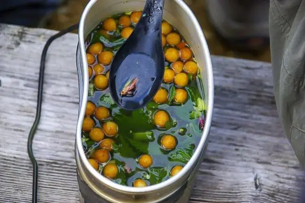 Grünes Wasser mit gelben Früchten und einem Löffel in einem Behälter