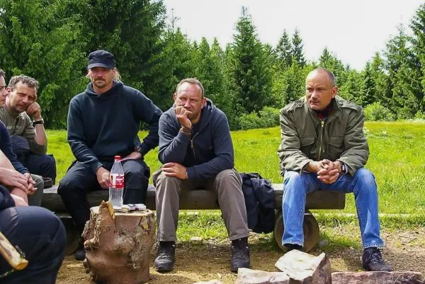 Gruppe sitzt auf Baumstämmen in der Natur, umgeben von Bäumen und Wiese