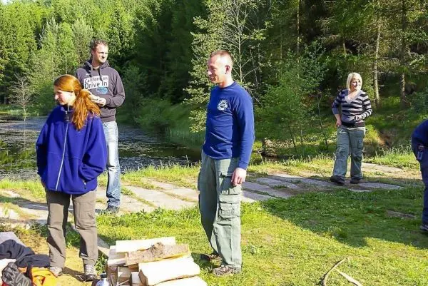Gruppe steht am Ufer eines Gewässers, Holzstapel im Vordergrund
