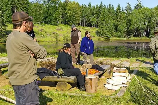 Gruppe steht um eine Holzbank, auf der Ausrüstung und Holzstücke liegen