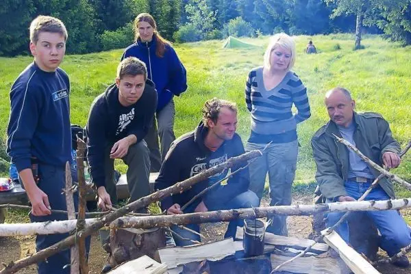 Gruppe um ein Feuer mit einem Kessel auf einem improvisierten Gestell aus Ästen