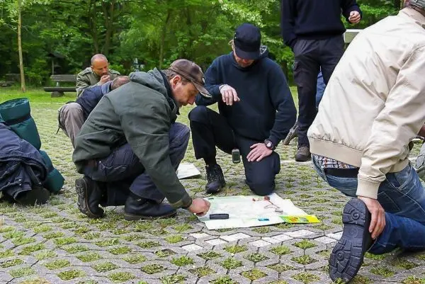 Gruppenteilnehmer knien um eine Karte und analysieren diese gemeinsam