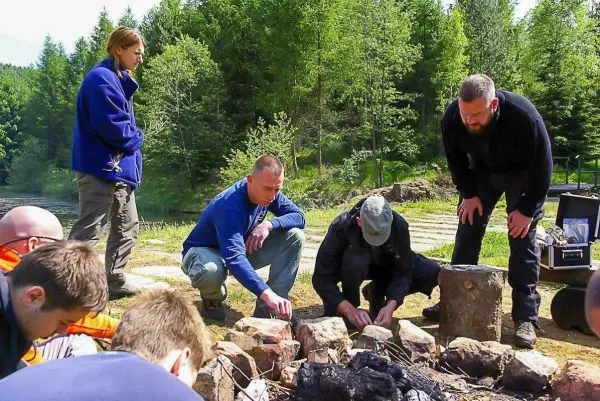 Gruppierung um ein kleines Bodenfeuer, Holzstücke werden arrangiert