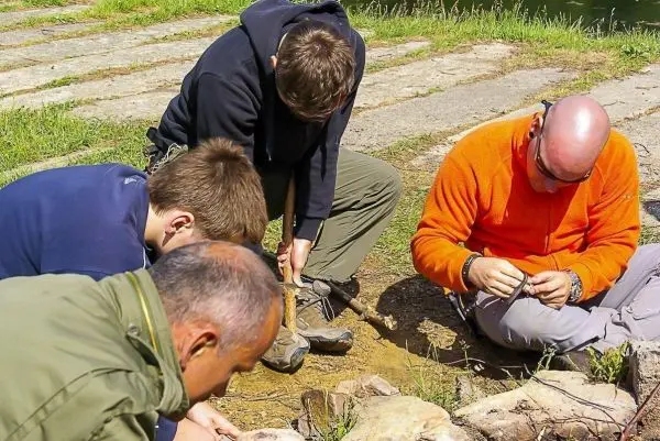 Gruppierung von vier Personen um ein Feuerstelle, während sie Zunder vorbereiten