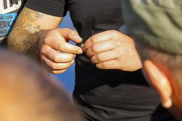 Hände halten ein kleines Objekt, während andere Personen im Hintergrund aufmerksam schauen