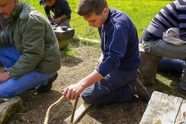 Junge bearbeitet Holz mit einem selbstgebauten Werkzeug beim Überlebenstraining