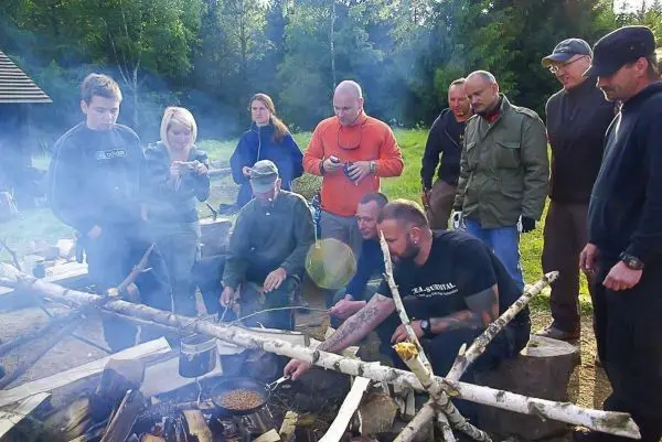 Kessel über offenem Feuer wird mit Holz befeuert, mehrere Personen beobachten das Geschehen