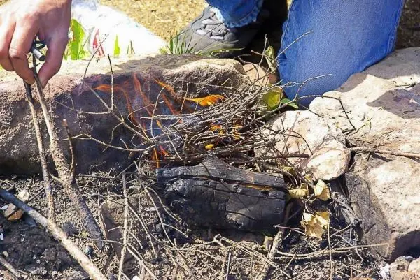 Kleine Flamme glimmt zwischen Ästen und Holzstücken im Feuerkreis