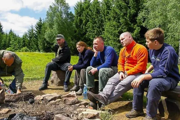 Lagerfeuer mit Steinen umgeben, Teilnehmer sitzen auf Holzstämmen