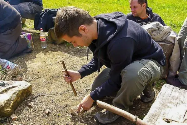 Mann bearbeitet Holzstück mit einem Stock zur Feuererzeugung