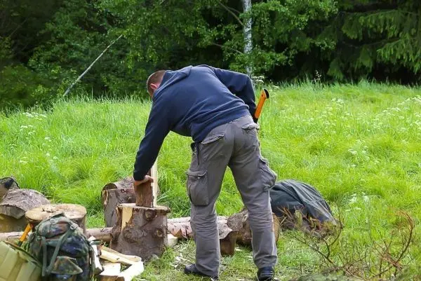 Mann bearbeitet Holzstücke mit einer Axt in einer grünen Wiese