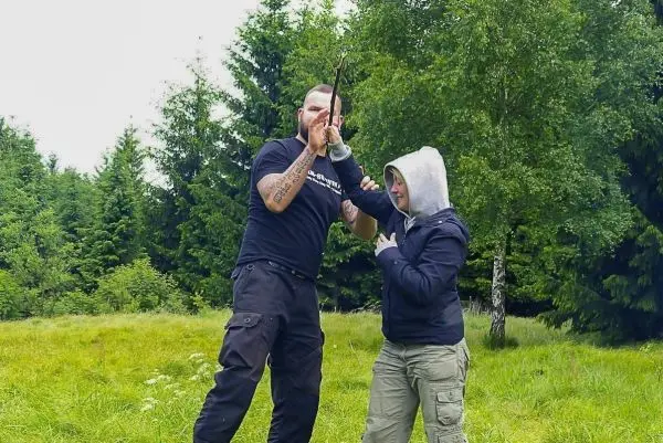 Mann demonstriert Technik mit improvisierter Waffe an Frau im Freien