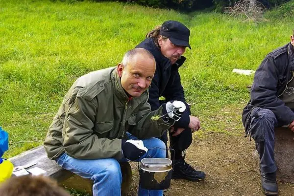 Mann hält einen Kessel mit einer Schnur in der Hand, sitzt auf einer Bank