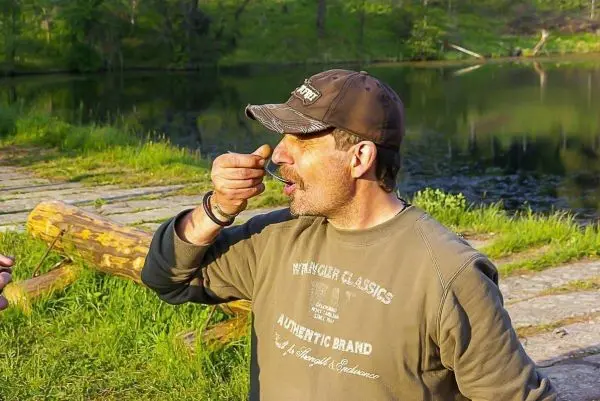 Mann hält einen Löffel an den Mund am Ufer eines Gewässers