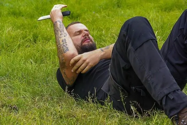 Mann liegt auf Gras und hält ein Messer in der Hand