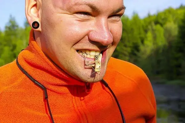 Mann mit orangefarbener Jacke lächelt, während ein Insekt an seinem Mund hängt