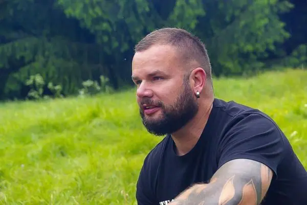 Mann mit tätowiertem Arm sitzt auf dem Gras und schaut nachdenklich