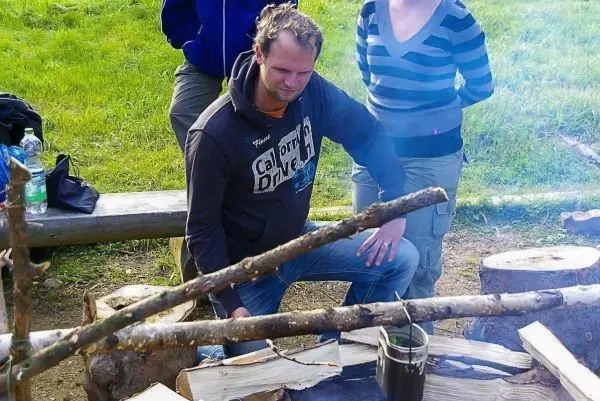 Mann sitzt neben einem Feuer und überwacht einen Kessel über der Flamme