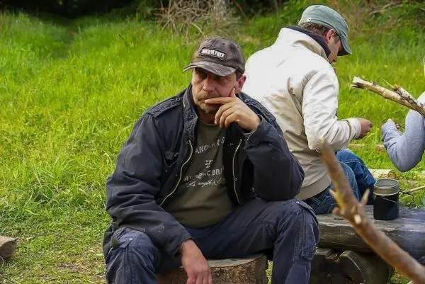 Person sitzt nachdenklich auf einem Baumstumpf im Freien