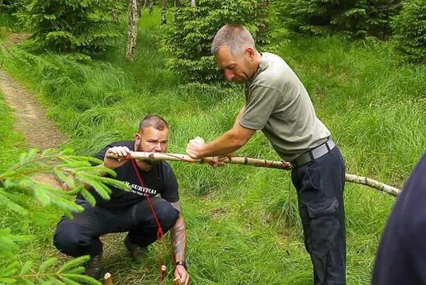 Zwei Personen bearbeiten einen Stock im Wald beim Überlebenstraining