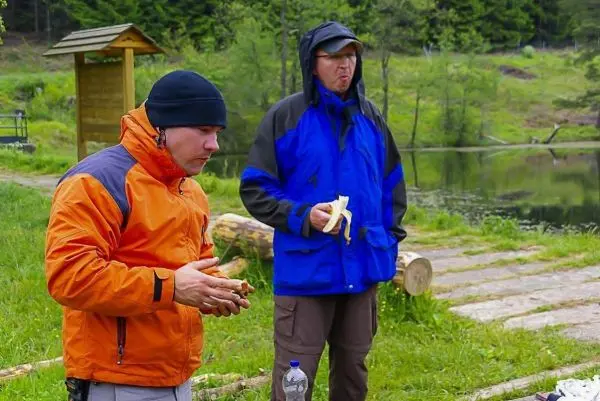Zwei Personen essen an einem Gewässer, einer hält eine Banane in der Hand