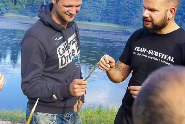 Zwei Personen halten einen Stock und diskutieren am Ufer eines Gewässers