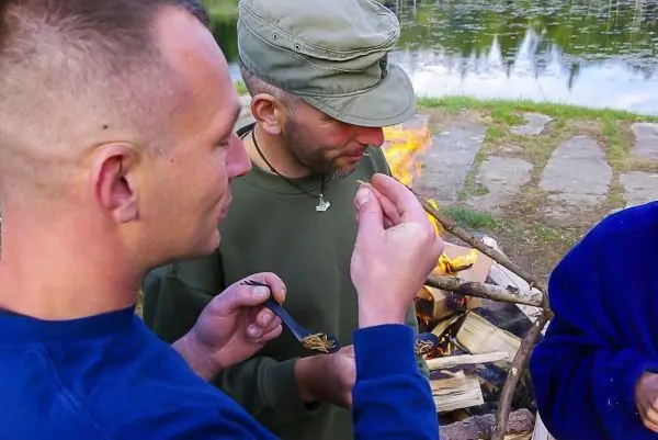 Zwei Personen halten Essen über einem Feuer und unterhalten sich
