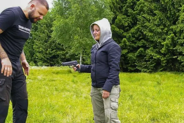 Zwei Personen im Freien, eine Person hält eine Pistole in Richtung der anderen