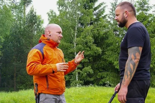 Zwei Personen im Gespräch, eine trägt eine orange Jacke, die andere hält einen Stock