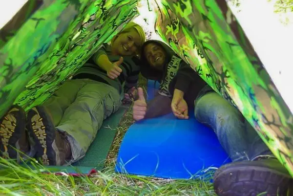 Zwei Personen liegen in einer Tarp-Notunterkunft und zeigen Daumen hoch