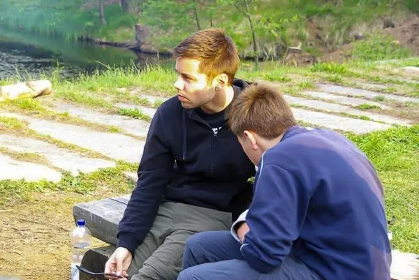 Zwei Personen sitzen auf einer Holzbank am Ufer eines Gewässers