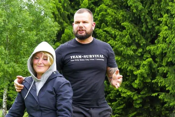 Zwei Personen stehen im Freien vor grünen Bäumen, eine Person spricht