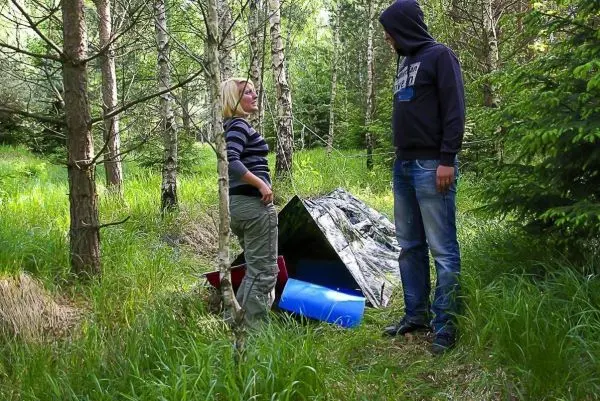 Zwei Personen stehen neben einer improvisierten Tarp-Notunterkunft im Wald