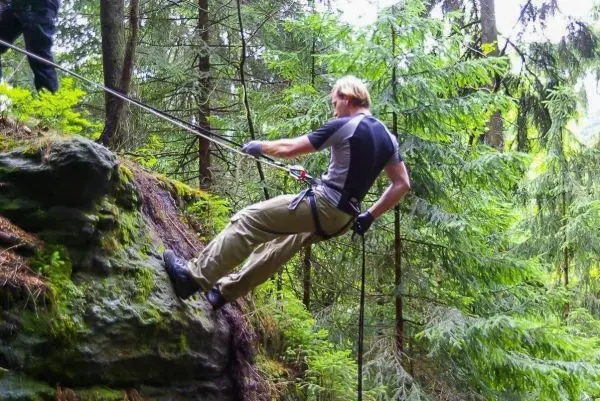 Abseilen an einem Felsvorsprung mit Seil und Karabiner im Wald