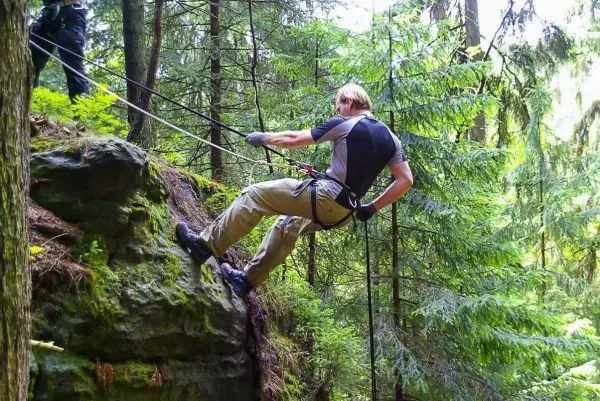 Abseilen an einer Felswand mit Seil und Sicherungshaken im Wald