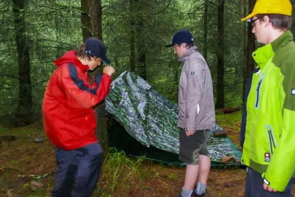 Drei Personen bauen eine Tarp-Notunterkunft im Wald auf