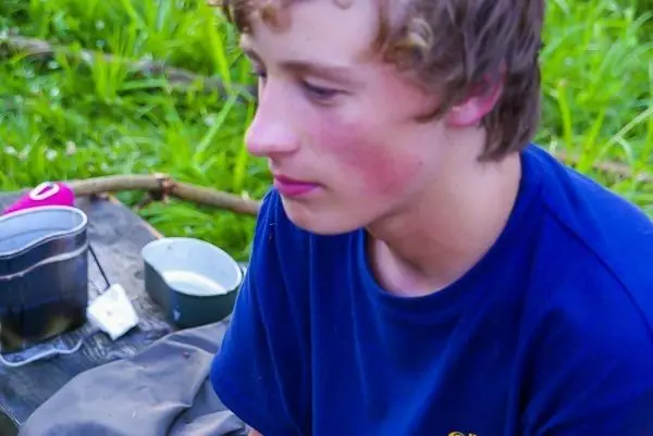 Ein Junge sitzt neben einem Holzstück mit einem Kochtopf und einer Tasse