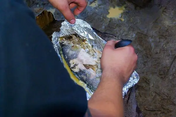 Fisch wird in Alufolie auf einem Holzstück zubereitet
