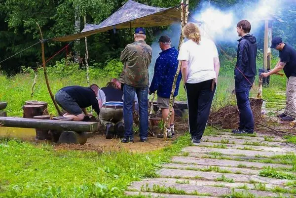 Gruppe arbeitet an einem Feuerplatz unter einem Tarp, Rauch steigt auf