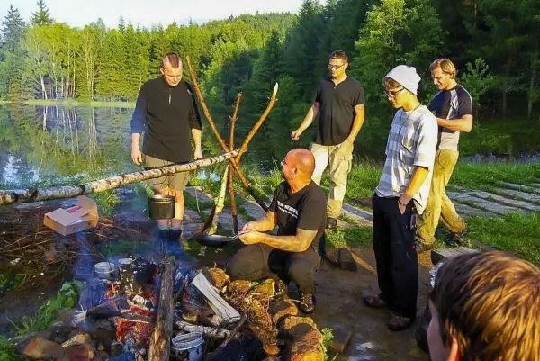 Gruppe um ein Lagerfeuer mit Kochtopf über der Flamme