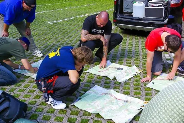 Gruppenteilnehmer analysieren Karten auf dem Boden, einige nutzen Kompasse zur Orientierung