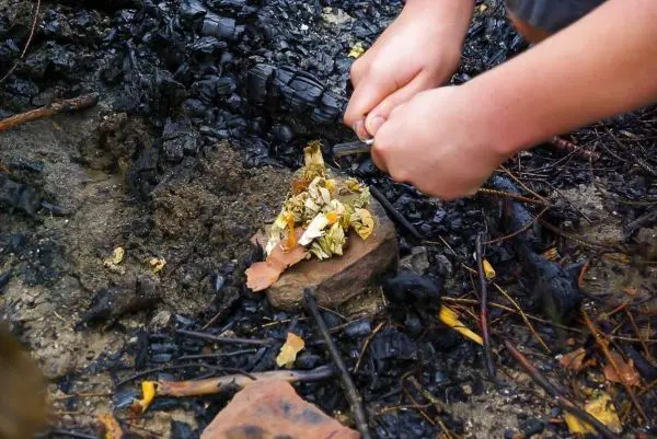 Hände zündeln Zunder auf einem Stein in einer verbrannten Umgebung