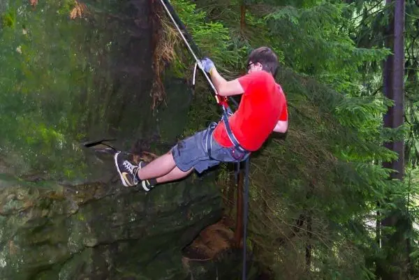 Junge seilt sich an einem Felsvorsprung mit Sicherungsseil ab
