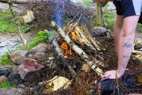 Kleine Flamme brennt zwischen Holzstücken und Ästen auf dem Boden