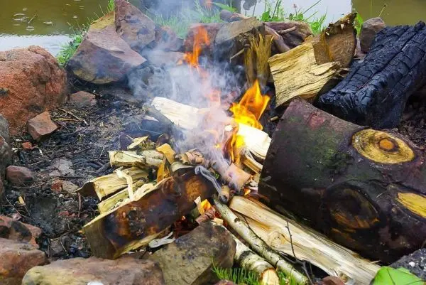 Kleine Flamme zwischen Holzstücken, Rauch steigt auf