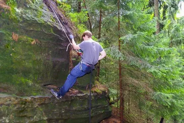 Kletterer sichert sich mit Seil an einer Felswand im Wald